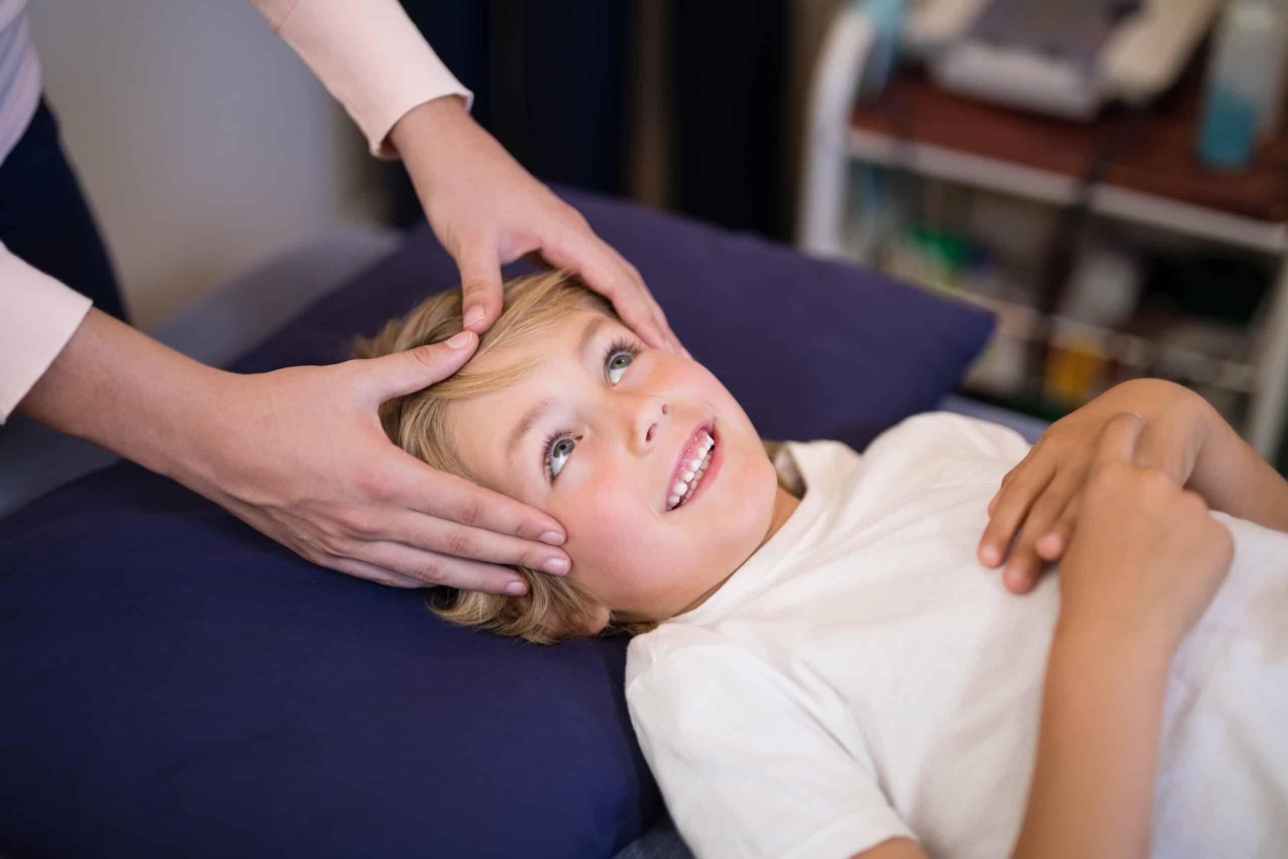 Cropped hands of female therapist giving head massage to boy lying on bed at hospital ward