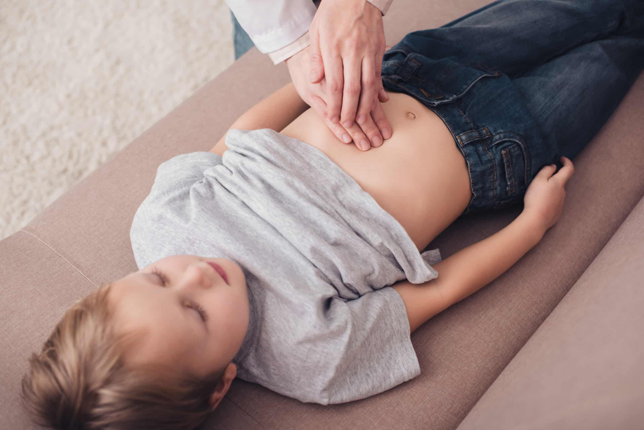 cropped image of pediatrist palpating sick boy stomach on sofa in living room