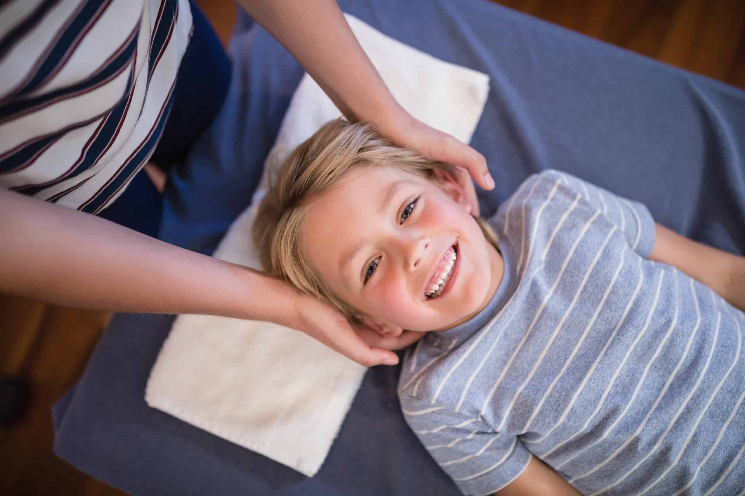 High angle portrait of smiling smiling boy receiving massage from female physiotherapist at hospital ward
