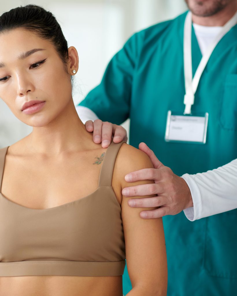 Rehab center worker palpating shoulder of sportswoman suffering with chronic pain after injury